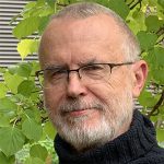 Headshot of Mark Haxthausen in front of green leaves.
