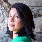 headshot of Mari Binnie wearing a green sweater and standing in front of a stone wall