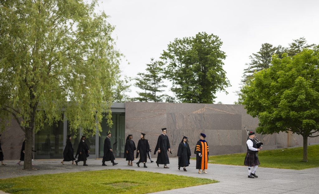 graduating students led by a bagpiper through the clark's grounds as part of their hooding ceremony